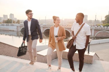 Neşeli genç çoklu etnik öğrenciler üniversite merdivenlerinden çıkıp sınıfları tartışıyorlar.