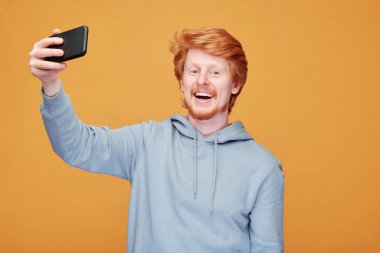 Kapüşonlu genç kızıl sakallı blogcu portresi turuncu arka planda reklamlar yaparken kenara çekiyor.