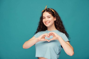 Kıvırcık saçlı, gözlerini kısarak bakan, yüzünü mavi arka planda ekşiten çılgın güzel kız.