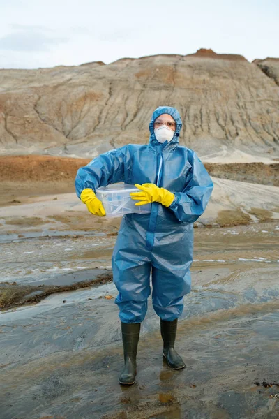 穿着防护服 呼吸器 橡胶手套和靴子的年轻女科学家 他们拿着装有水和土壤样本的塑料容器 — 图库照片