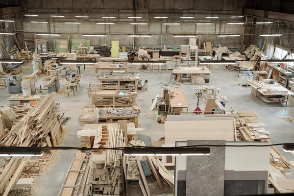 Workbench of furniture factory worker with wooden workpieces, electric handtools and other stuff surrounded by various equipment