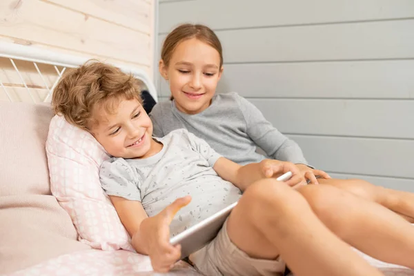 幸せなかわいい男の子と彼の幸せな妹でホームウェアでオンライン漫画を見ながらリラックスしながらベッドで週末に自宅 — ストック写真