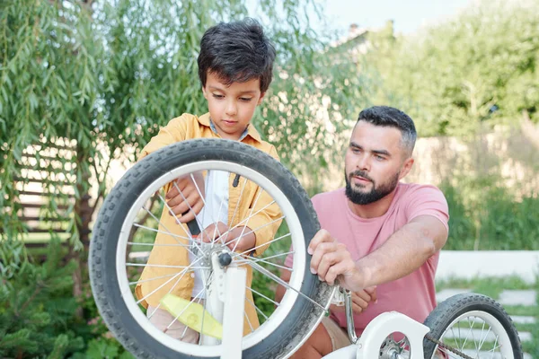 Młody Ojciec Trzyma Rower Podczas Gdy Jego Mały Syn Próbuje — Zdjęcie stockowe