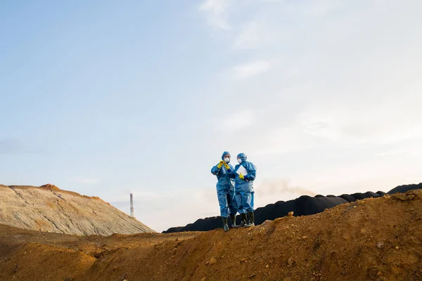 两名女性研究人员站在山顶上调查被污染土壤和空气污染的荒芜地区时的小数字 — 图库照片