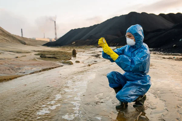 有毒地区的当代年轻女性生态学家或防护工作服和呼吸器研究人员将土壤样本放入瓶中 — 图库照片