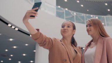 Alışveriş merkezinde alışveriş yaptıktan sonra gülen ve poz veren genç kadınların düşük açı takibi.