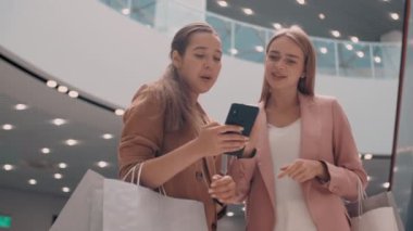 Alışveriş merkezinde durup sohbet ederken cep telefonuna bakan mutlu genç kız arkadaşlarının düşük açılı görüntüleri.