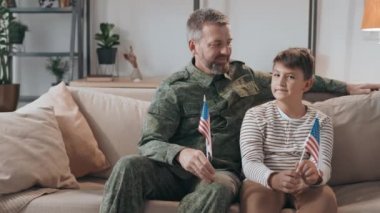 Askeri üniformalı orta yaşlı bir erkek subayın portresi ve oğlu kanepede oturmuş Amerikan bayrakları taşıyor.