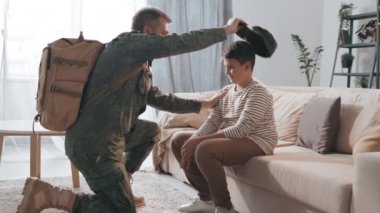 Askeri üniformalı bir erkek subayın oğlunun önünde diz çöktüğü ve göreve gitmeden önce ona veda ettiği orta boy bir fotoğraf.