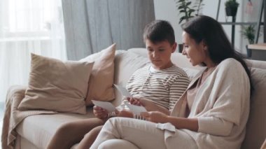 Oturma odasında kanepede oturan ve fotoğraflara bakan genç bir kadınla orta boy bir fotoğraf.