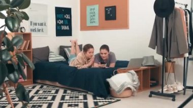 Rahat bir odada, yatakta uzanmış, cep telefonuna bakarken sohbet eden genç kız arkadaşlarının çekimleri.
