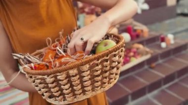 Açık havada duran, şeker toplamaya çıkanları beklerken sepetteki şeker ve elmalara bakan tanınmayan genç bir kadının el kamerasıyla çekilmiş görüntüsü.