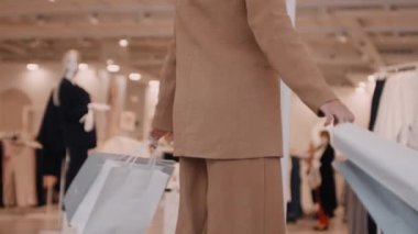 Alışveriş torbaları tutan ve kameraya gülümseyen genç bayanın yavaşça eğilmesi.