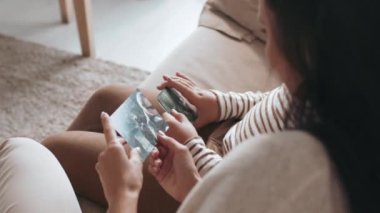 Oturma odasındaki kanepede oturan genç bir kadın ve tanınmayan bir çocuğun omuz üstü fotoğrafı.