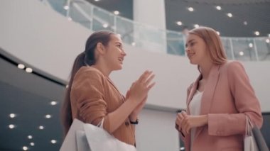 Alışveriş merkezinde alışveriş torbalarıyla sohbet eden mutlu genç kadınların düşük açılı takibi