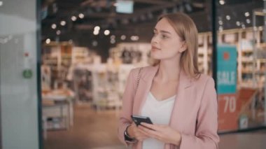 Alışveriş merkezinde yürüyen ve cep telefonu kullanan genç bir kadının yavaş takibi.