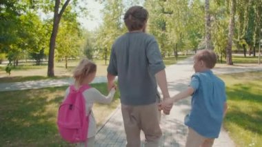 Tatlı kız ve çocukla el ele tutuşan ve güneşli yaz gününde parkta yürüyen bir adamın dikiz aynasıyla takip etmek.