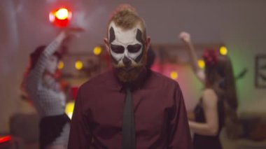 Cadılar Bayramı makyajlı neşeli bir genç adam portresi bıyığını çeviriyor ve ev partisinde kameraya poz veriyor.