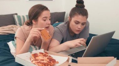 Genç kız arkadaşlarının birlikte yatakta yatarken ve bilgisayardan alışveriş yaparken çekilmiş bir fotoğrafı. Pizza onların yanında yatıyordu.