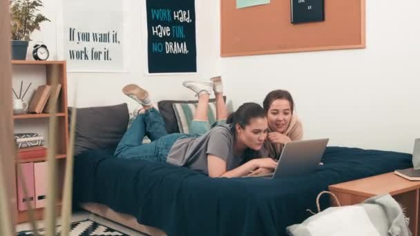 明るい若い女性の友人の撮影を追跡ベッドの上に彼らの居心地の良い大学寮の部屋とブラウジングインターネット上のラップトップ — ストック動画