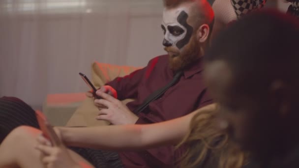 Handheld Slowmo Young People Sitting Couch Halloween Party Using Mobile — Stock Video