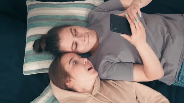手持式头像拍摄的快乐少女躺在床上 在手机上浏览互联网 他们在说话和笑 — 图库视频影像
