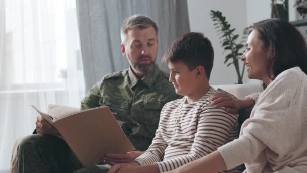 身着军服的男性军官与他的儿子和快乐的妻子坐在沙发上 阅读部署日志 — 图库视频影像
