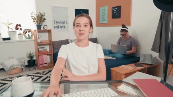 Povの女の子座っています彼女の机で大学寮と話上のビデオコールとして彼女の女性ルームメイトでヘッドフォンで作業ノートパソコンでバックグラウンド — ストック動画
