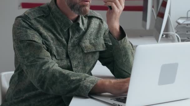 事務所の机に座って ウォーキートーキーを使用している間にラップトップを入力して制服を着た中年の男性米軍将校の遅いショットを傾ける — ストック動画