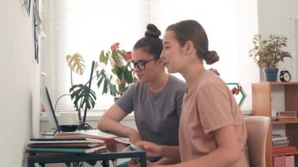 自宅や大学の寮の居心地の良い部屋で机の上に座っている陽気な若い女性の側面図と遠隔学習中のビデオ通話で話して — ストック動画