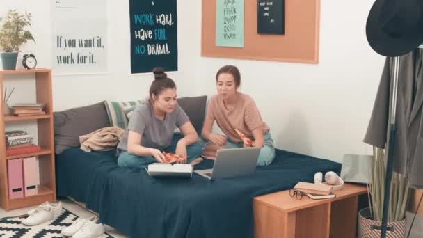 追踪快乐的年轻女性朋友们在舒适的房间里盘腿坐在床上 一边吃披萨 一边笑着 一边在笔记本电脑上看东西的镜头 — 图库视频影像