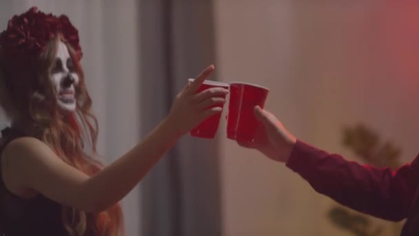 ハロウィンメイクをした幸せな男と若い女性の手持ち撮影自宅パーティーでアルコールでプラスチックカップをクリックし 飲みます — ストック動画