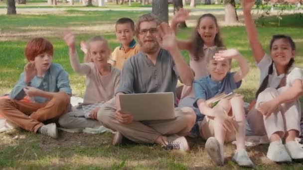 Портрет Счастливого Бородатого Учителя Ноутбуком Веселыми Школьниками Сидящими Траве Парке — стоковое видео