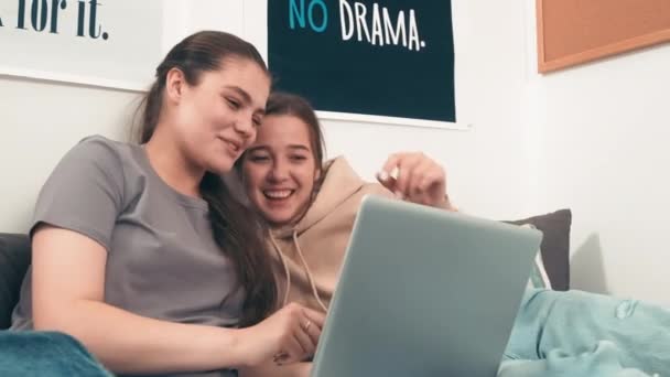 追踪调查快乐的年轻女性朋友在大学宿舍里躺在床上 一边笑一边看笔记本电脑上的东西的照片 — 图库视频影像