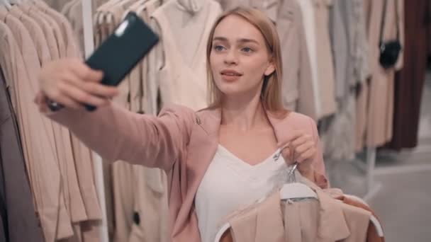 慢慢地 快乐的年轻女人拿着衣架 一边微笑着一边在商店里买东西 — 图库视频影像