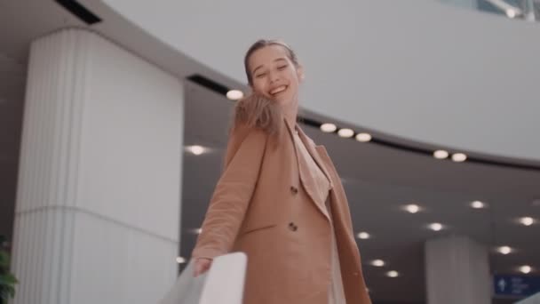 在商场里 一个快乐的年轻女子拿着购物袋笑着在相机前纺纱时的低角度镜头 — 图库视频影像