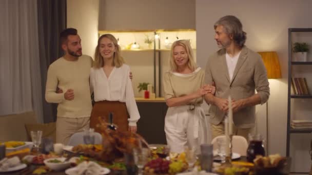 感謝祭の夕食のテーブルの近くに来て 何かについて話す幸せな若いカップルとその両親 — ストック動画