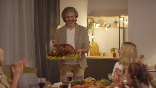 快乐的中年男人带着大大的烤火鸡参加感恩节大餐 他快乐的家人拍手叫好 镜头拍得很慢 — 图库视频影像