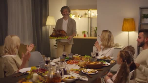 时尚成熟的男人带着大大的烤火鸡参加感恩节大餐 他快乐的家人拍手 慢镜头 — 图库视频影像