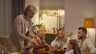 Neşeli, olgun bir adam Şükran Günü 'nü kutlarken kızarmış hindi kesip ailesi için pişiriyor.