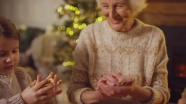 Kapalı süveter giyen, el işi kağıtları buruşturan çocukların büyükannenize Noel oyuncakları ve süslemeleri süslemesinde yardım etmesi.