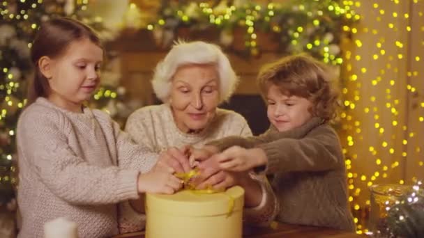 Średnie Ujęcie Miłej Babci Uczącej Dzieci Wiązać Kokardkę Pudełku Świątecznym — Wideo stockowe