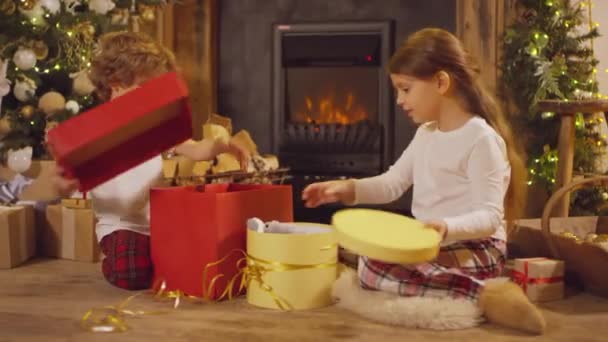 Два Маленьких Ребенка Сидят Друг Напротив Друга Распаковывая Рождественские Подарочные — стоковое видео