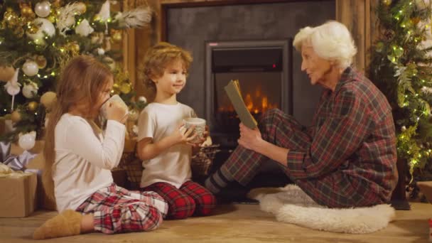 Małe Dzieci Piżamie Słuchające Babci Czytającej Książkę Wigilię Rozmawiającej Uśmiechającej — Wideo stockowe