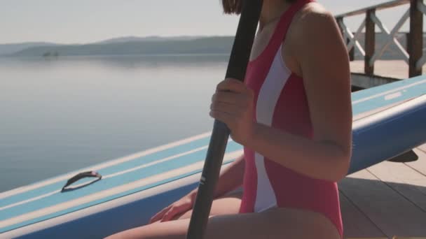晒黑的年轻女子手持桨坐在码头边缘的中等特写镜头 — 图库视频影像