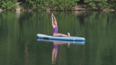 Açık denizde kürek çeken, yoga pozu veren, öne doğru eğilen bir kadın.