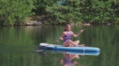 Gün ışığında yemek masasında oturan ve arka planda ağaçlarla kürek çeken güzel görünümlü bir kadın.