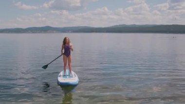 Dikiz aynasından sportif bir kadının kürek çekerken ve göl kıyısına yaklaşırken görüntüsü.