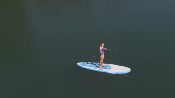 湖で一人でサーフィンを練習している女性のフィット感の高い角度のパンニング — ストック動画