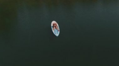 Terkedilmiş denizde kürek tahtasında uzanan sağlıklı bir kadının yoga egzersizi çekimleri.